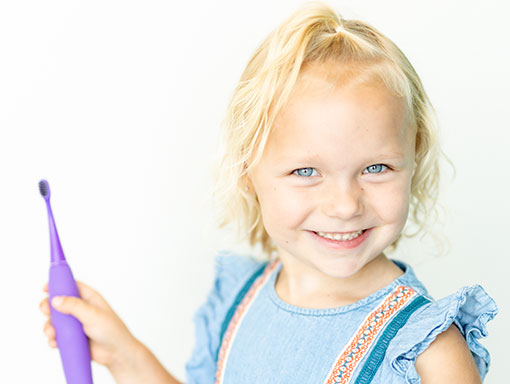 girl in blue holding toothbrush and smiling